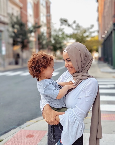 Drexel University physician assistant student Arkann Al-khalilee standing on a sidewalk holding her toddler son.